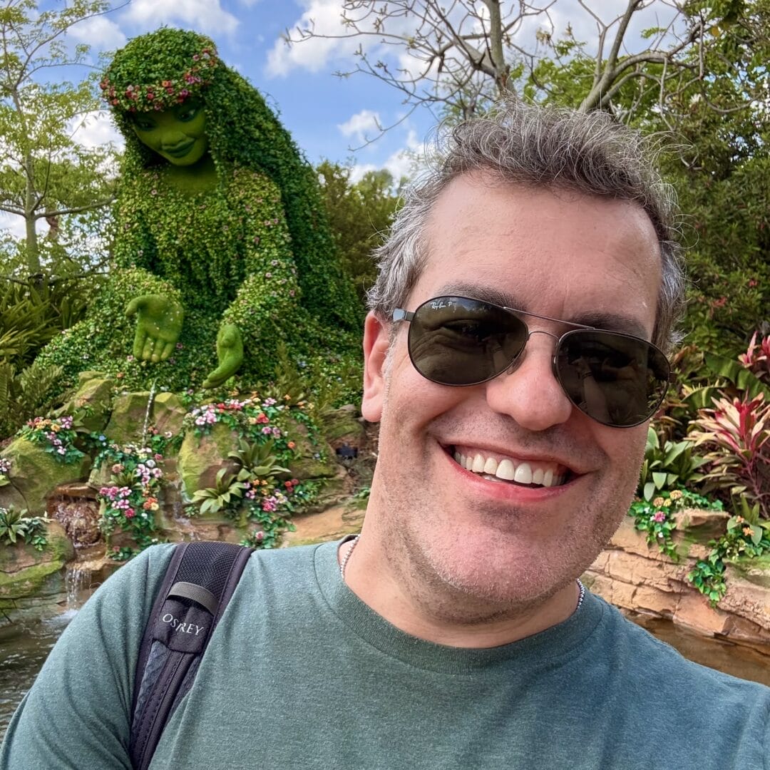 Photo of Chris Michaud, smiling while wearing sunglasses in front of a statue of Te Fiti from Moana